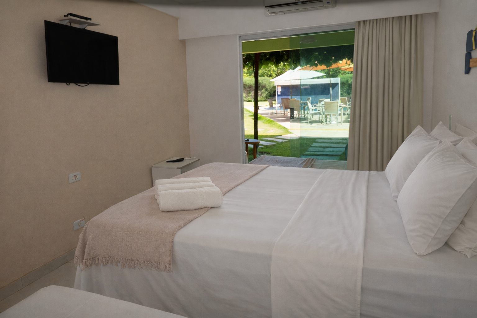 Quarto com três camas, um espelho e uma varanda com decoração em tons de verde vibrante.