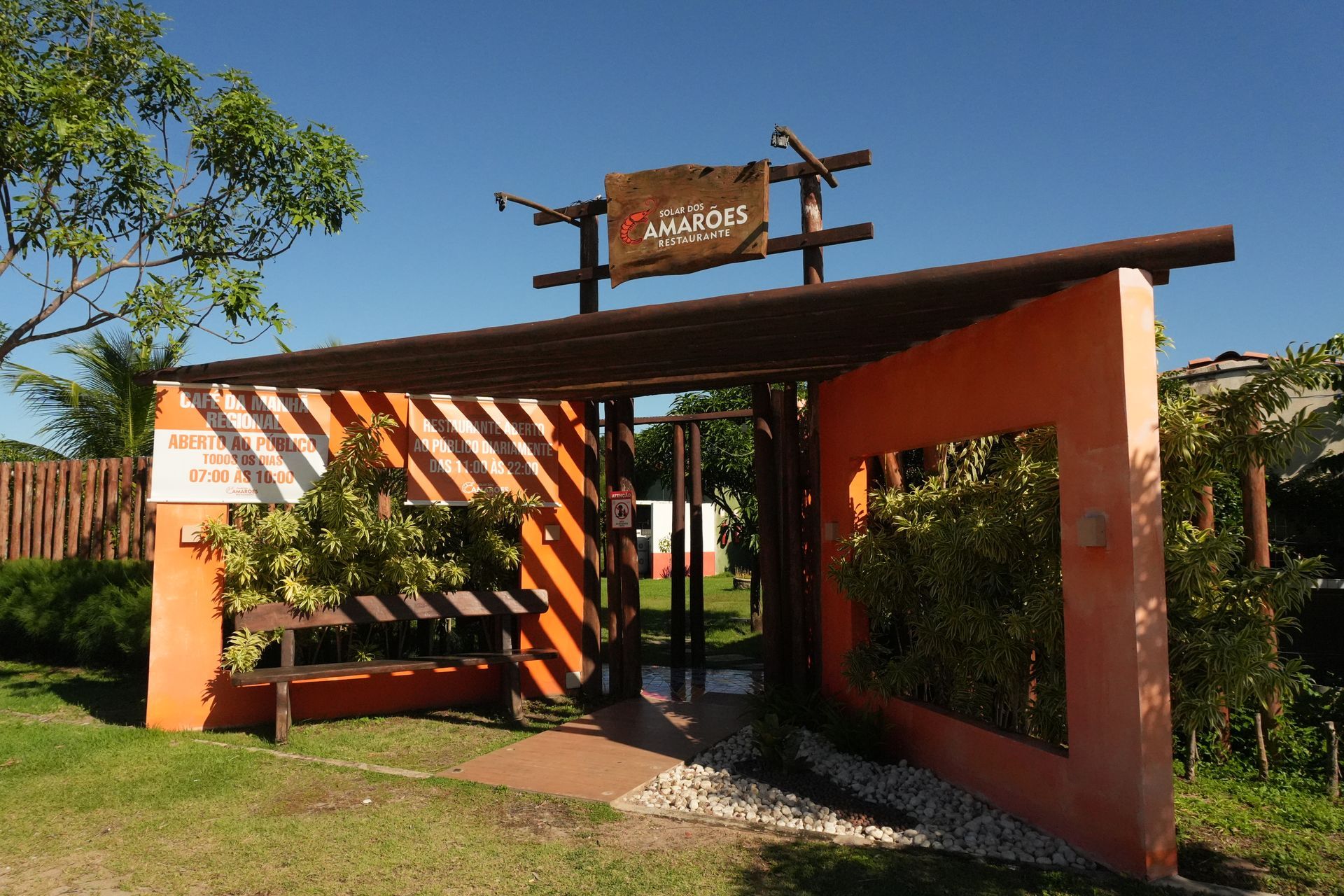 Entrada de um local com parede laranja, detalhes em madeira e uma placa.