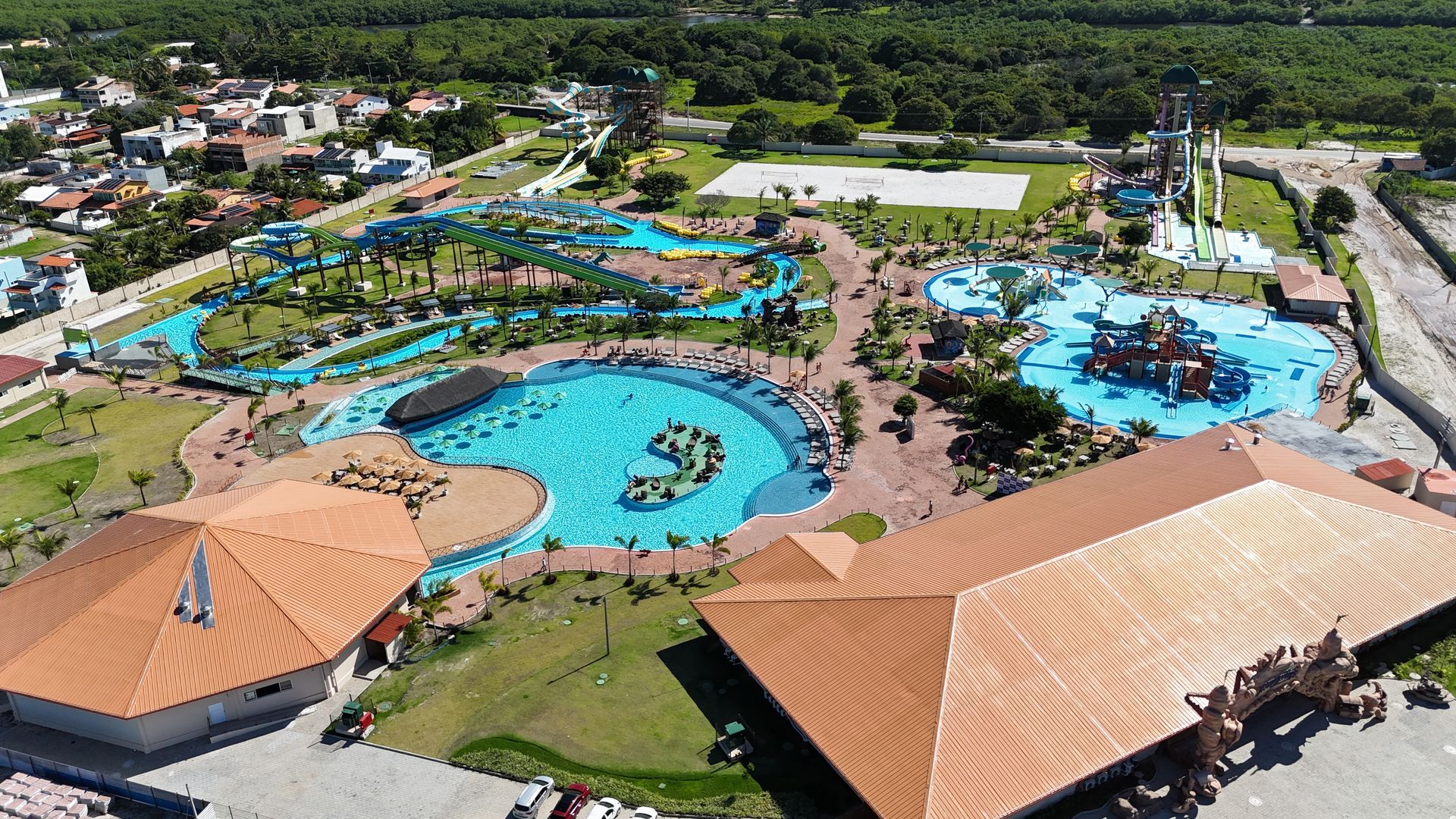 Vista aérea de um parque aquático com piscinas, toboáguas e edifícios. Uma vegetação exuberante circunda as atrações aquáticas.