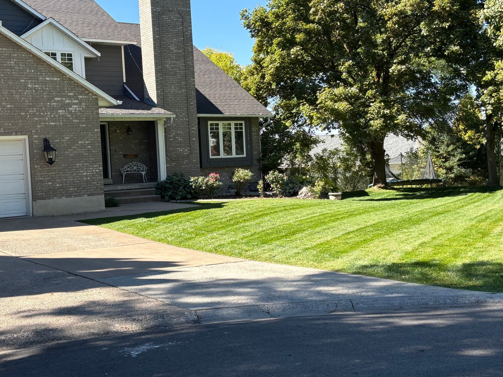 House with manicured lawn, stone chimney, and trees under a sunny sky.