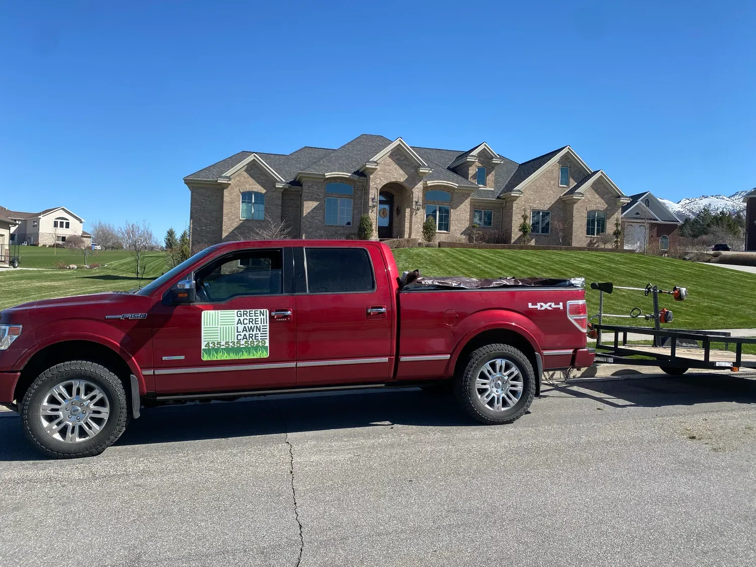 Red pickup truck with trailer parked in front of a brick house on a sunny day.