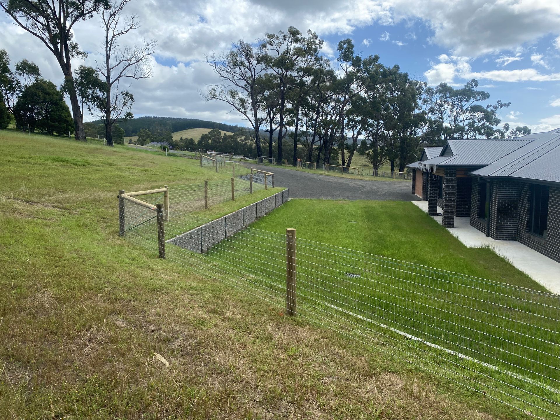 A fence surrounds a lush green field with a house in the background.
