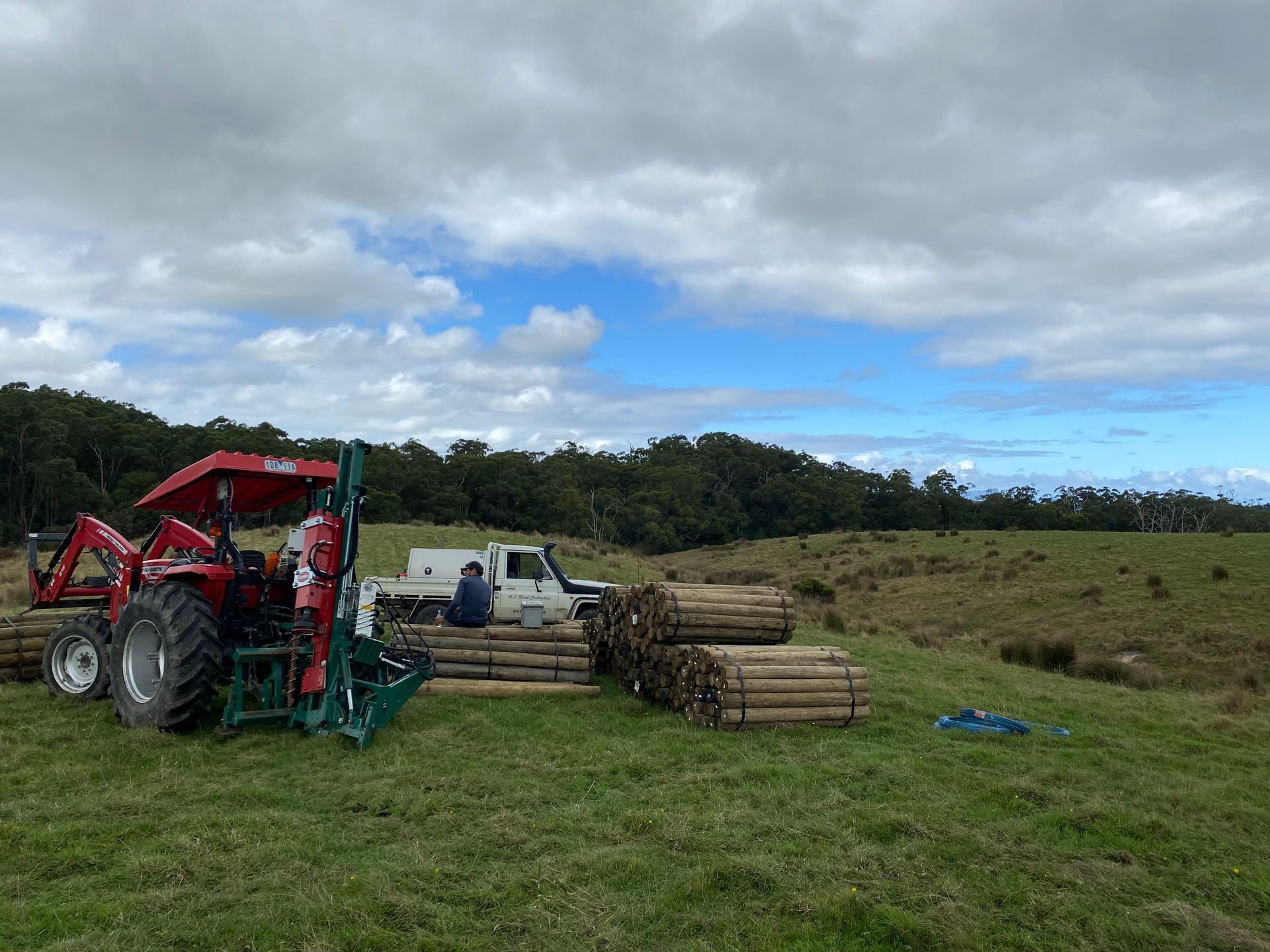 A red tractor is parked in a grassy field next to a pile of logs.