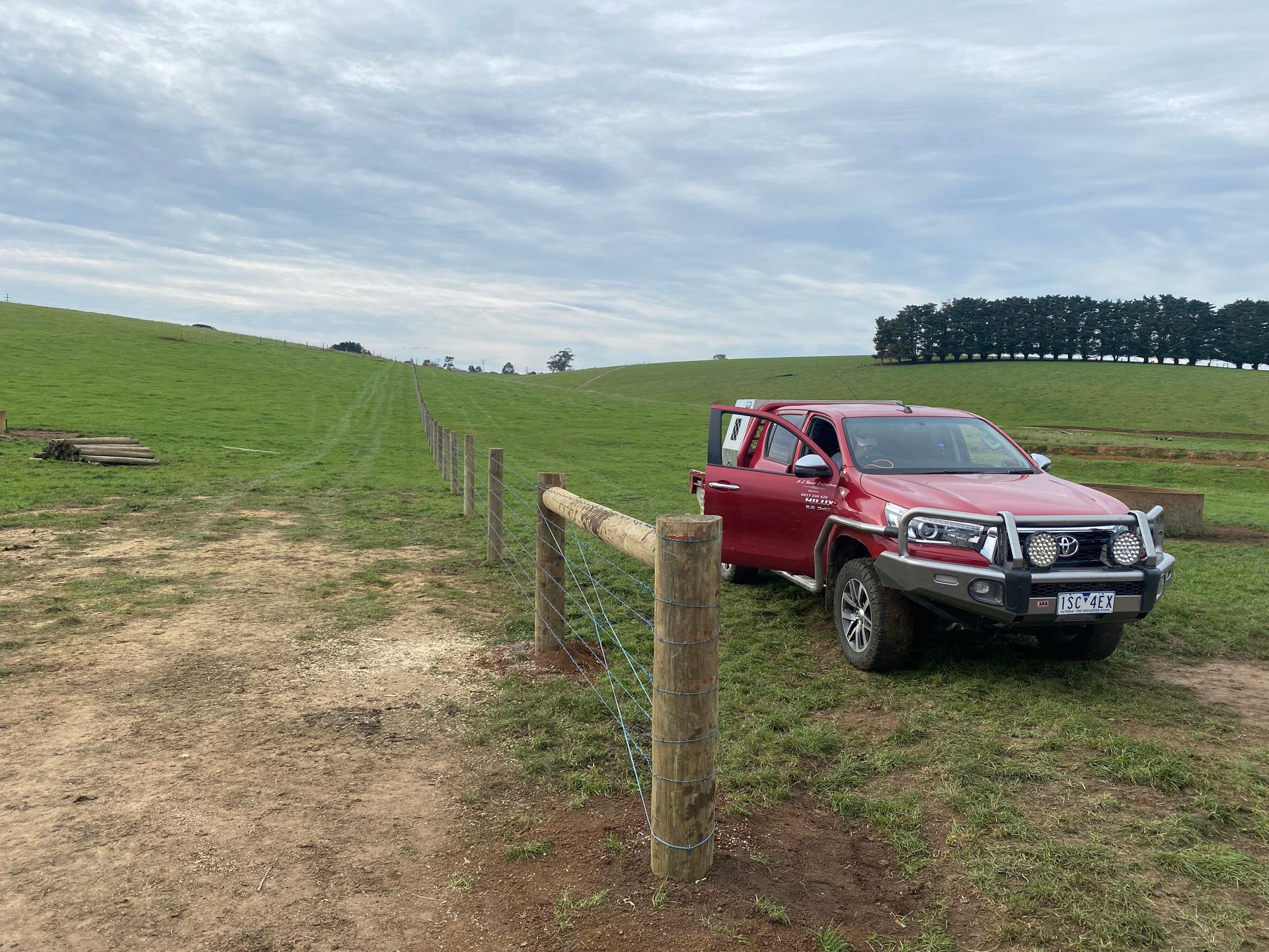A red truck is parked in a grassy field next to a wooden fence.