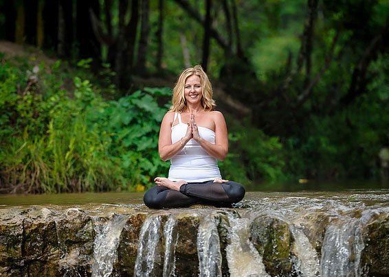 a woman is sitting in a lotus position on a rock next to a waterfall .