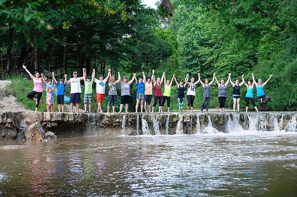 a group of people are standing on top of a waterfall holding hands .