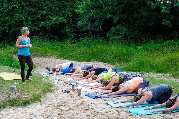 a woman is standing next to a group of people doing yoga on the beach .