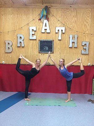 two women are standing next to each other on yoga mats in a yoga studio .