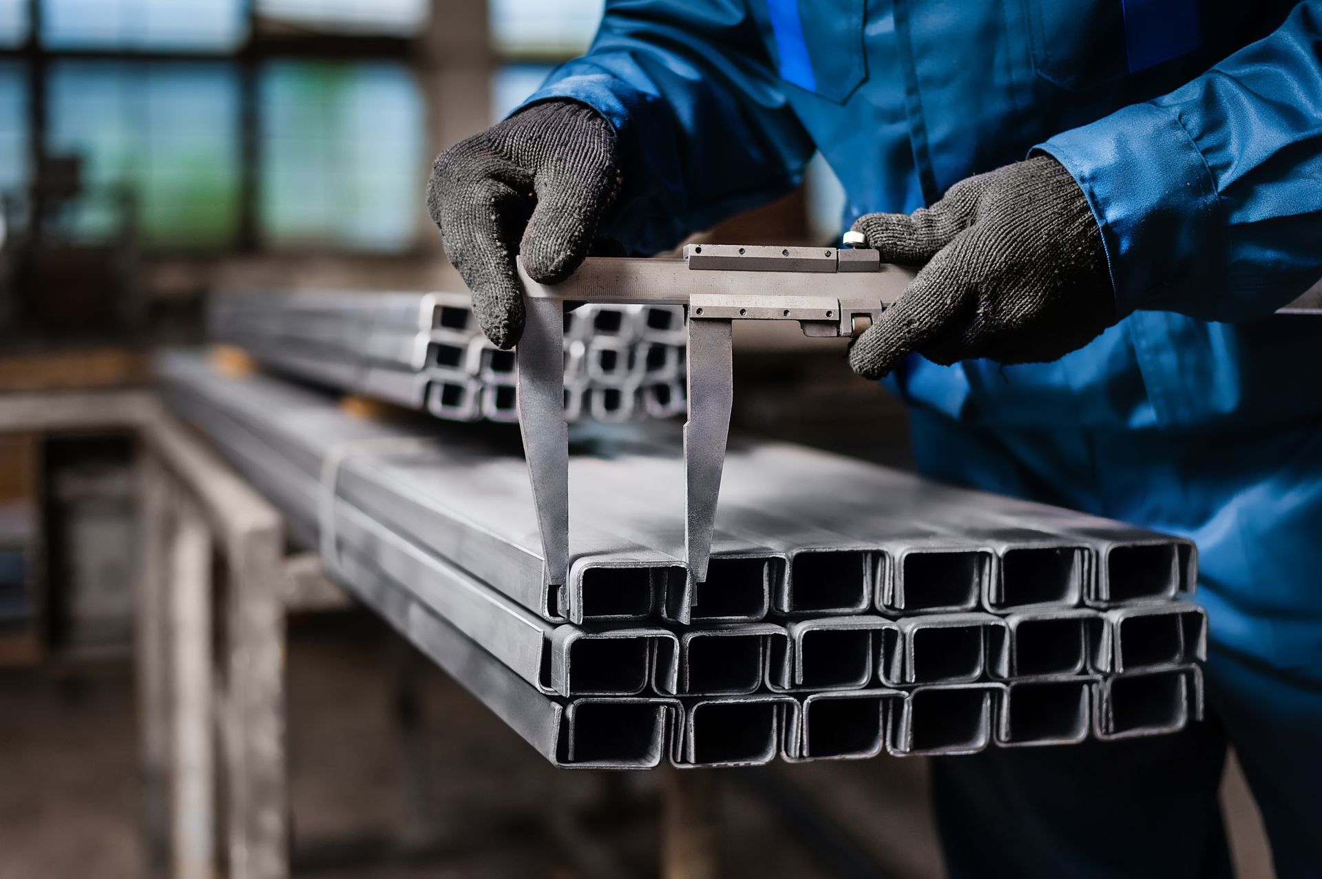 Worker measuring metal tubing with calipers in a steel fabrication shop.