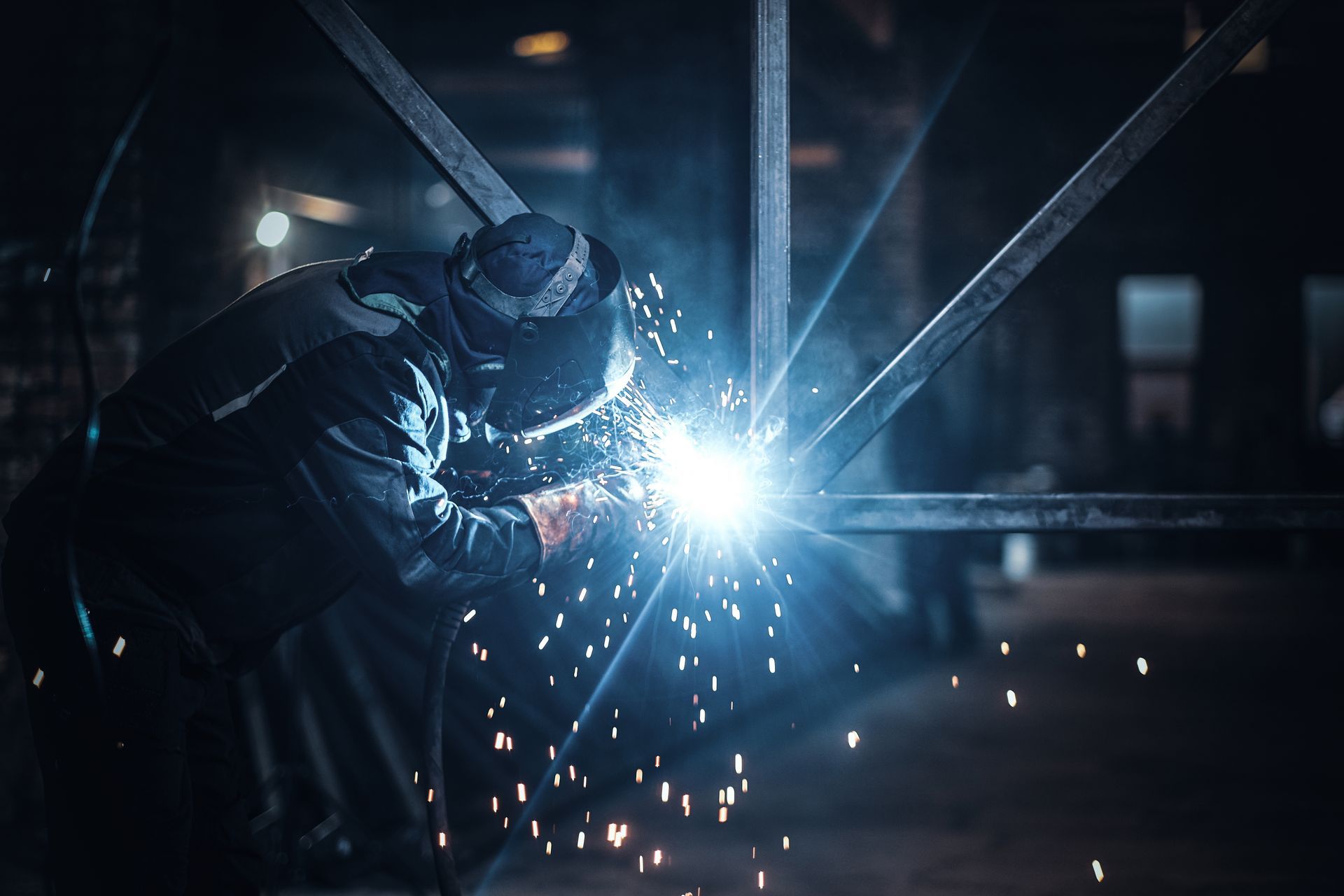 Welder working on a steel structure with bright sparks in a fabrication shop.