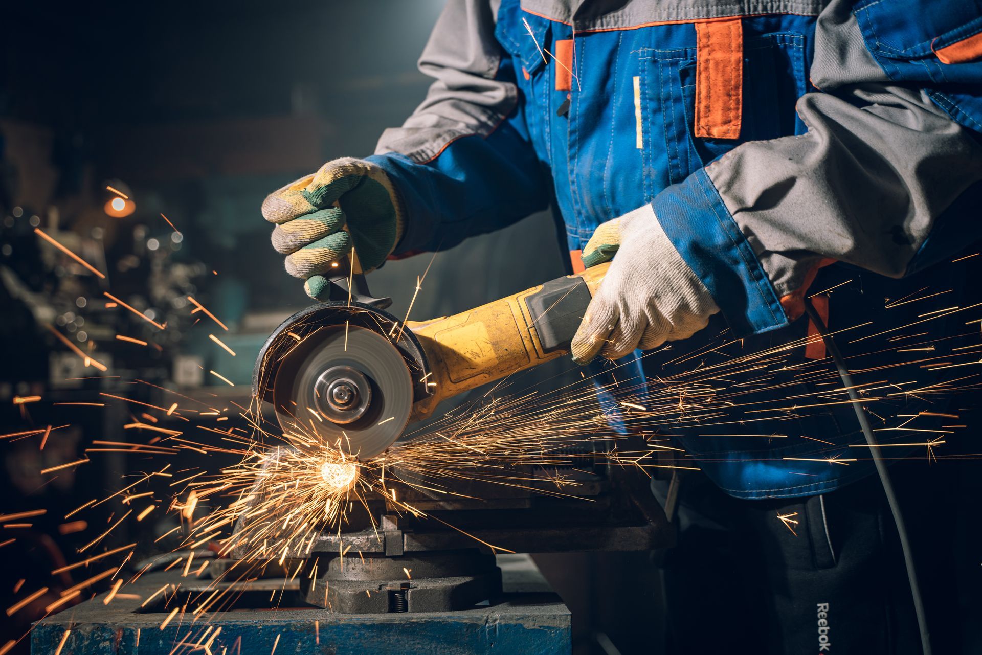 Person in blue work uniform grinding metal, sparks flying in workshop.