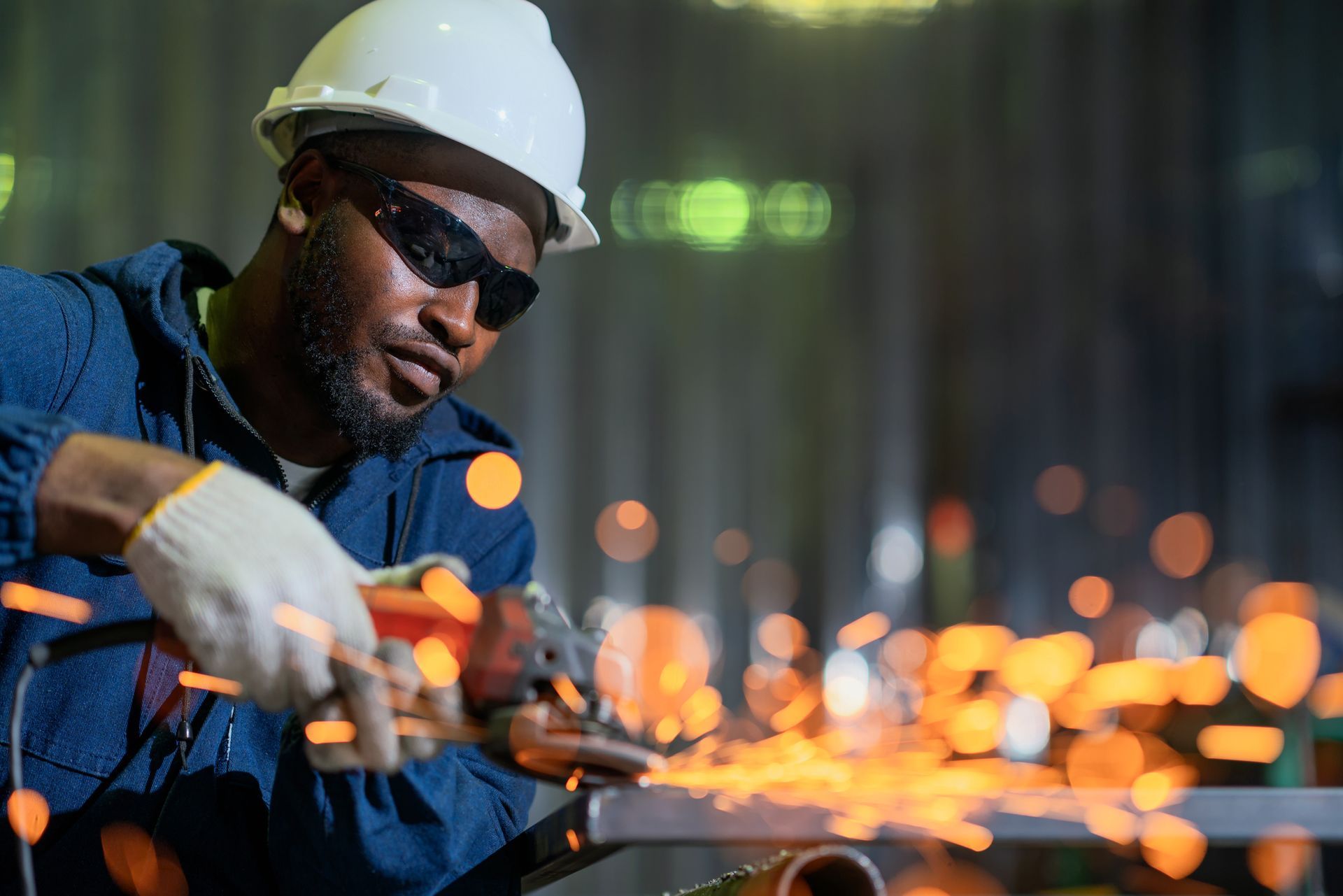 Worker grinding metal with sparks flying in a factory setting, wearing safety gear.