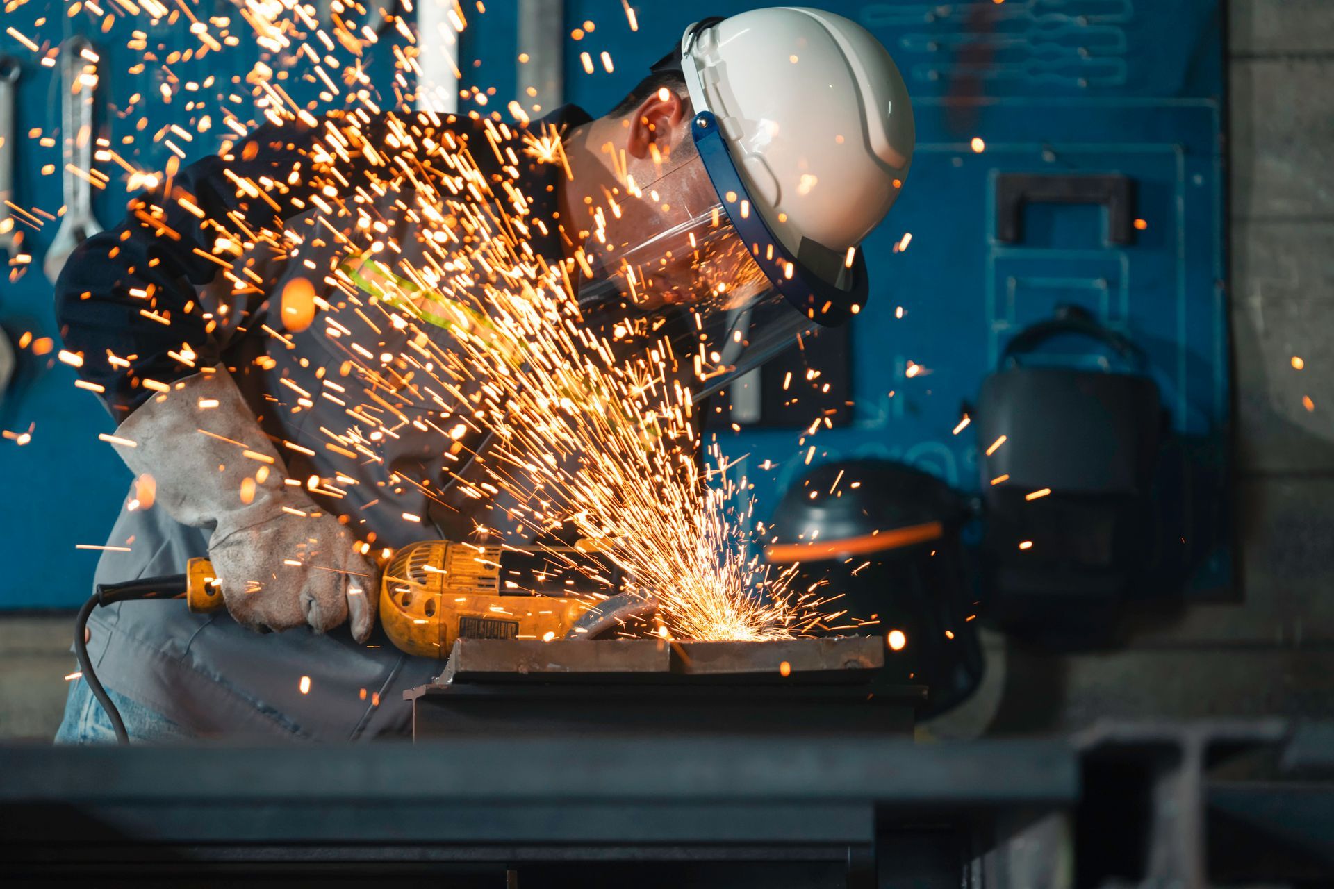 A worker in a safety helmet and gloves is using an angle grinder on a steel plate.
