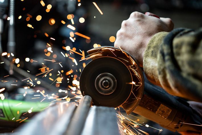Close-up of a male worker grinding metal, with sparks flying.