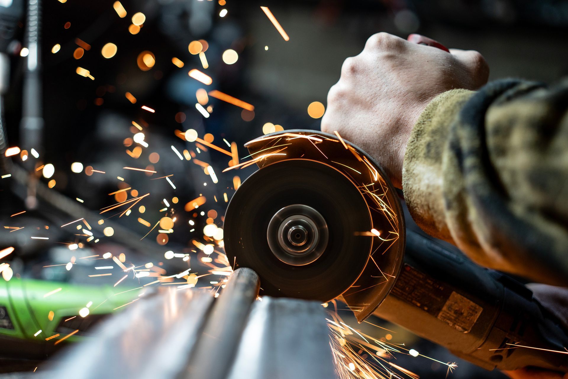 Hand using an angle grinder to cut metal with sparks flying.