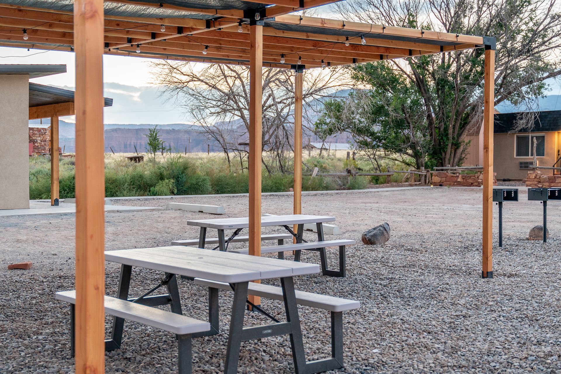 A group of picnic tables under a pergola in a gravel area.