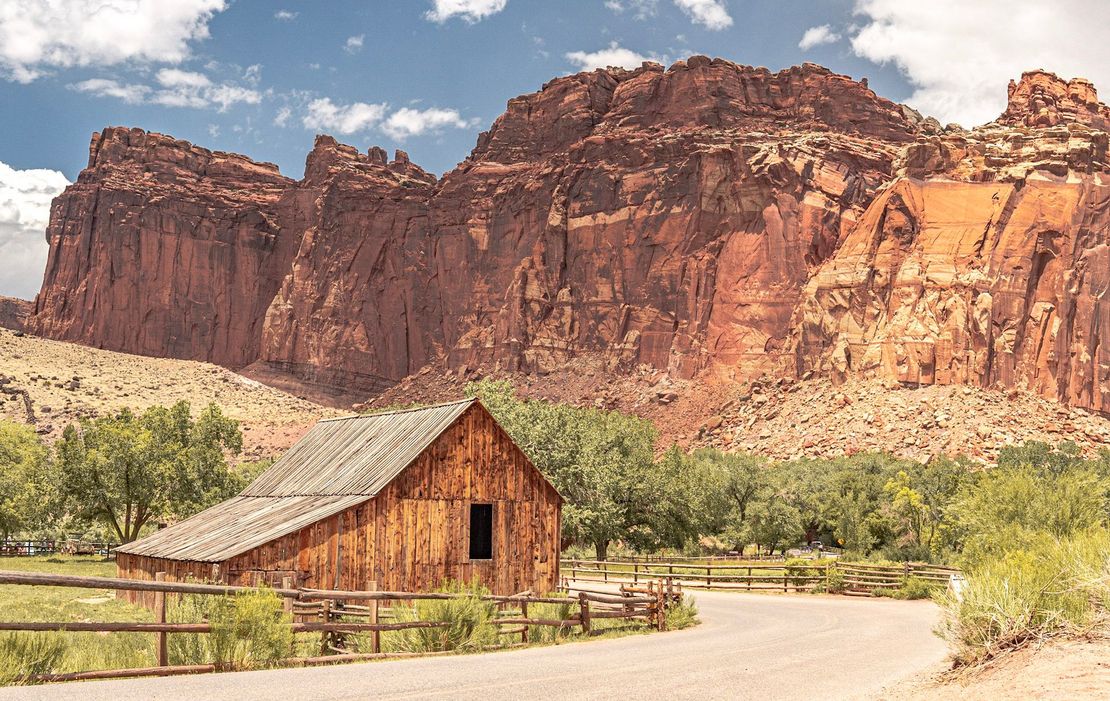 a wooden barn is sitting on the side of a dirt road in front of a mountain .