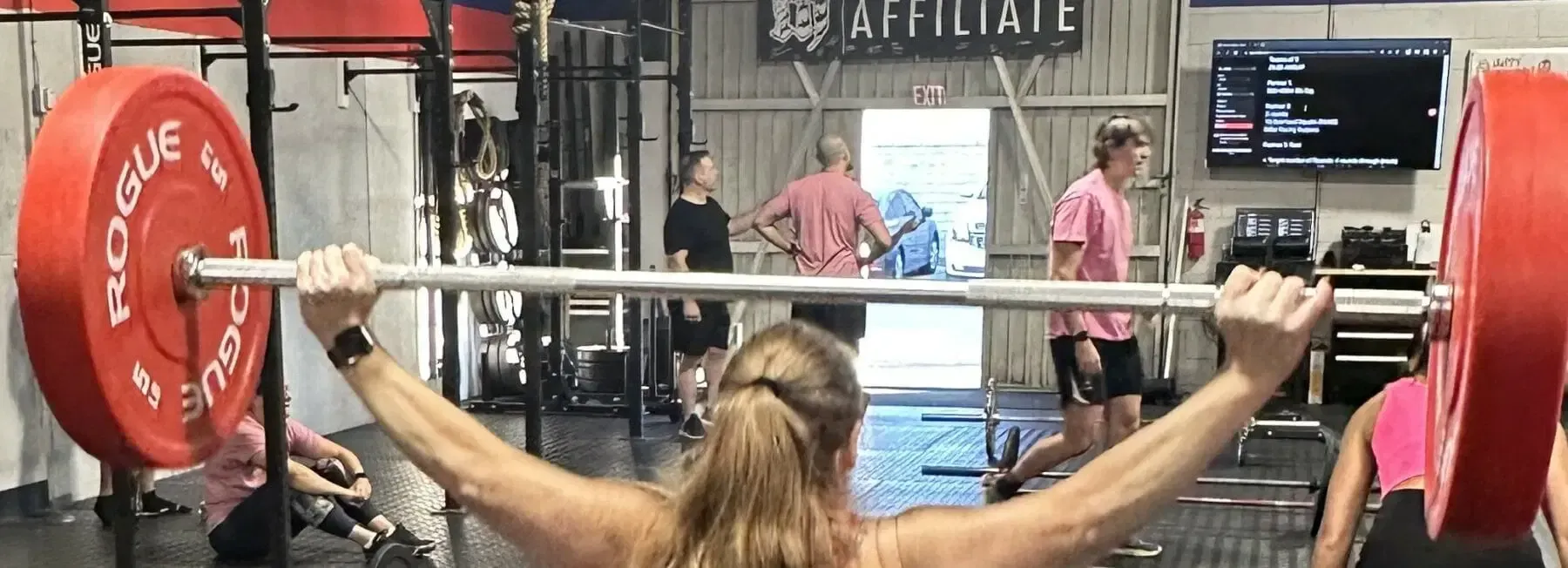 A woman is lifting a barbell over her head in a gym.