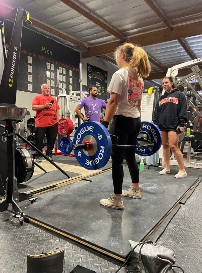 A woman is lifting a barbell in a gym.