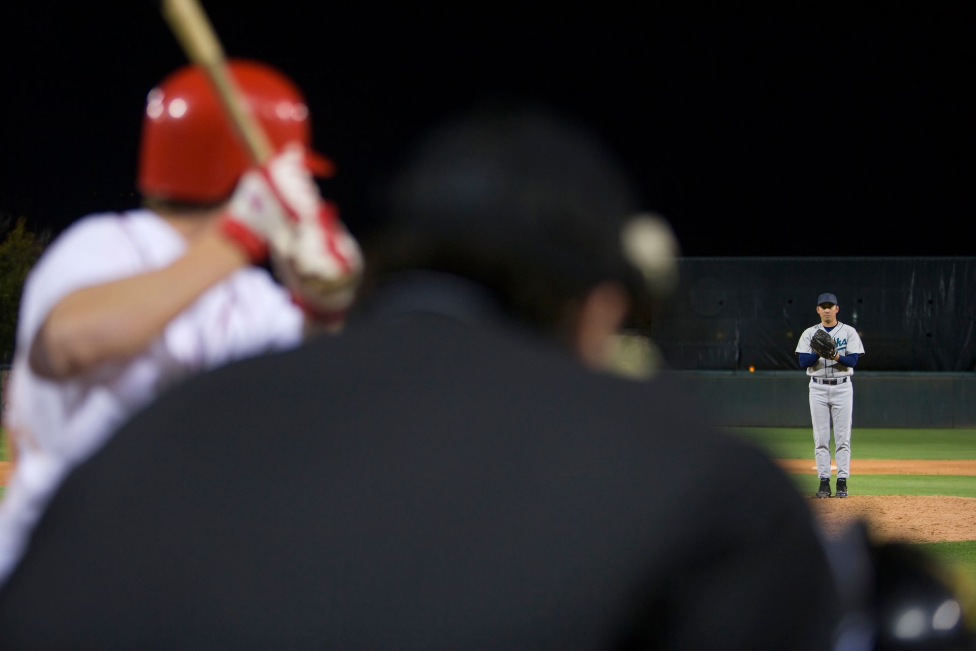 A baseball player in a red helmet holds a bat in front of an umpire