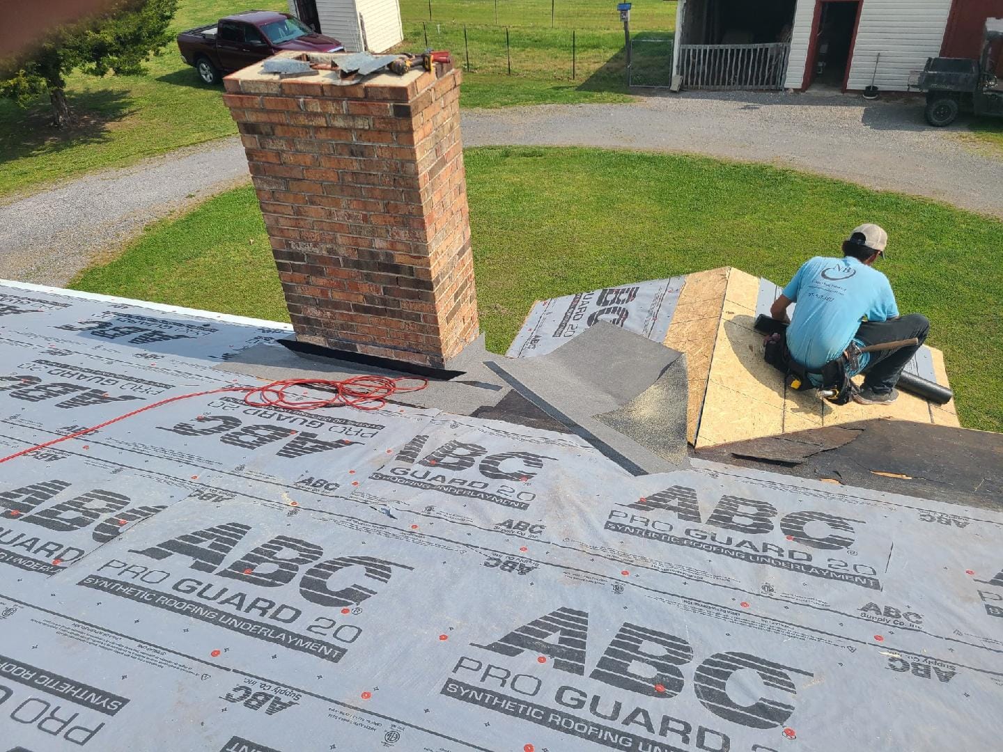 Roofer working on a roof with a brick chimney.  New roofing materials, including ABC Pro Guard 30, are laid out.