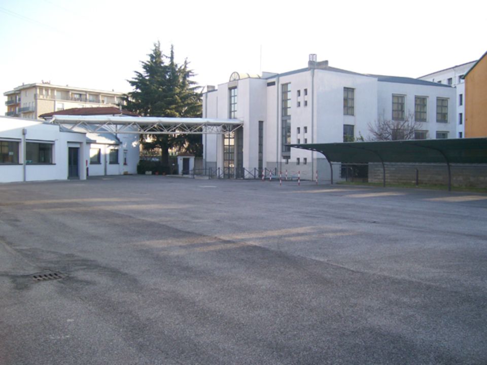 Parcheggio asfaltato vuoto di fronte a un edificio bianco con ingresso coperto.