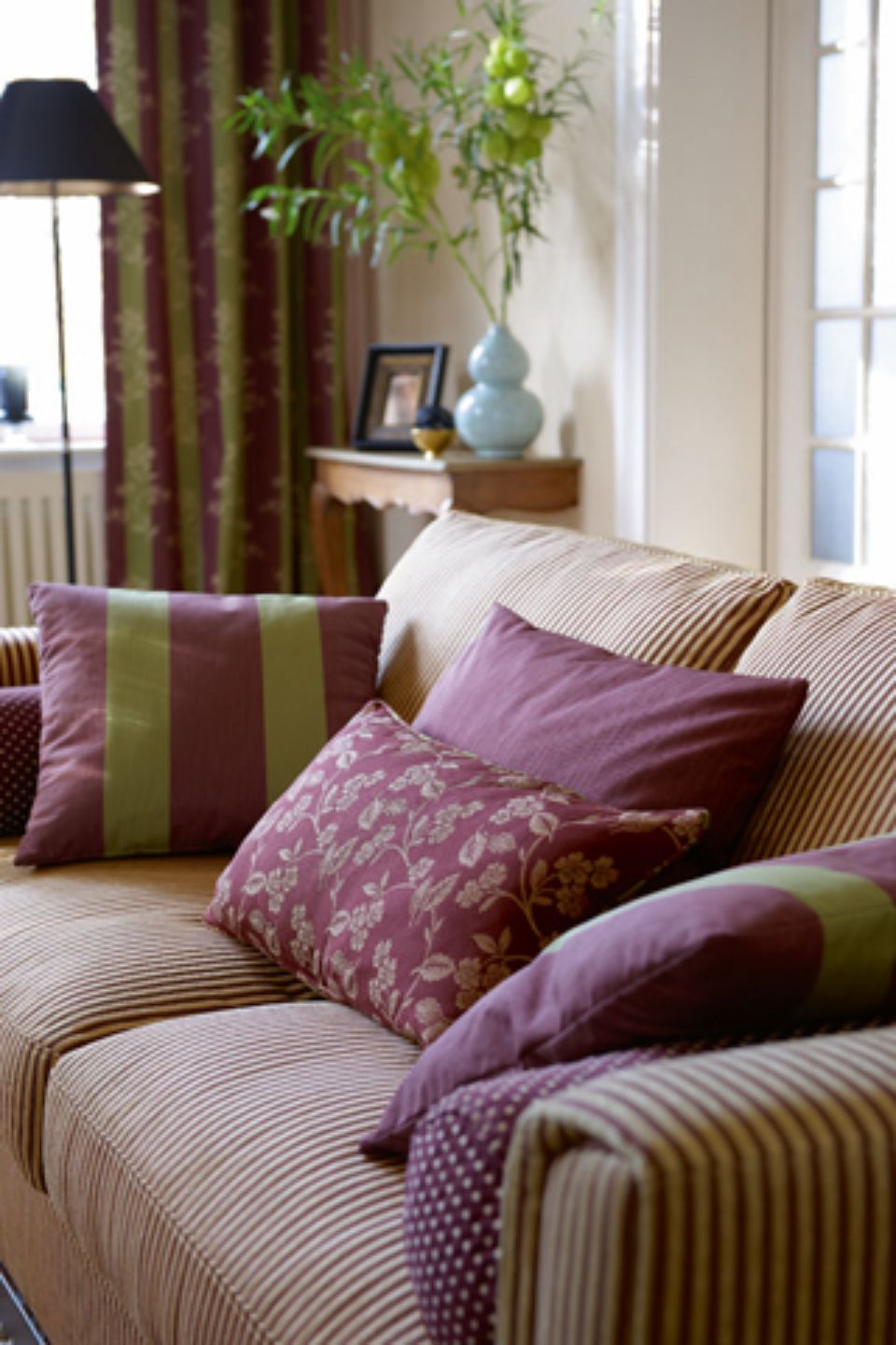 Divano con cuscini a righe, dettagli viola e verdi e tende in un soggiorno.