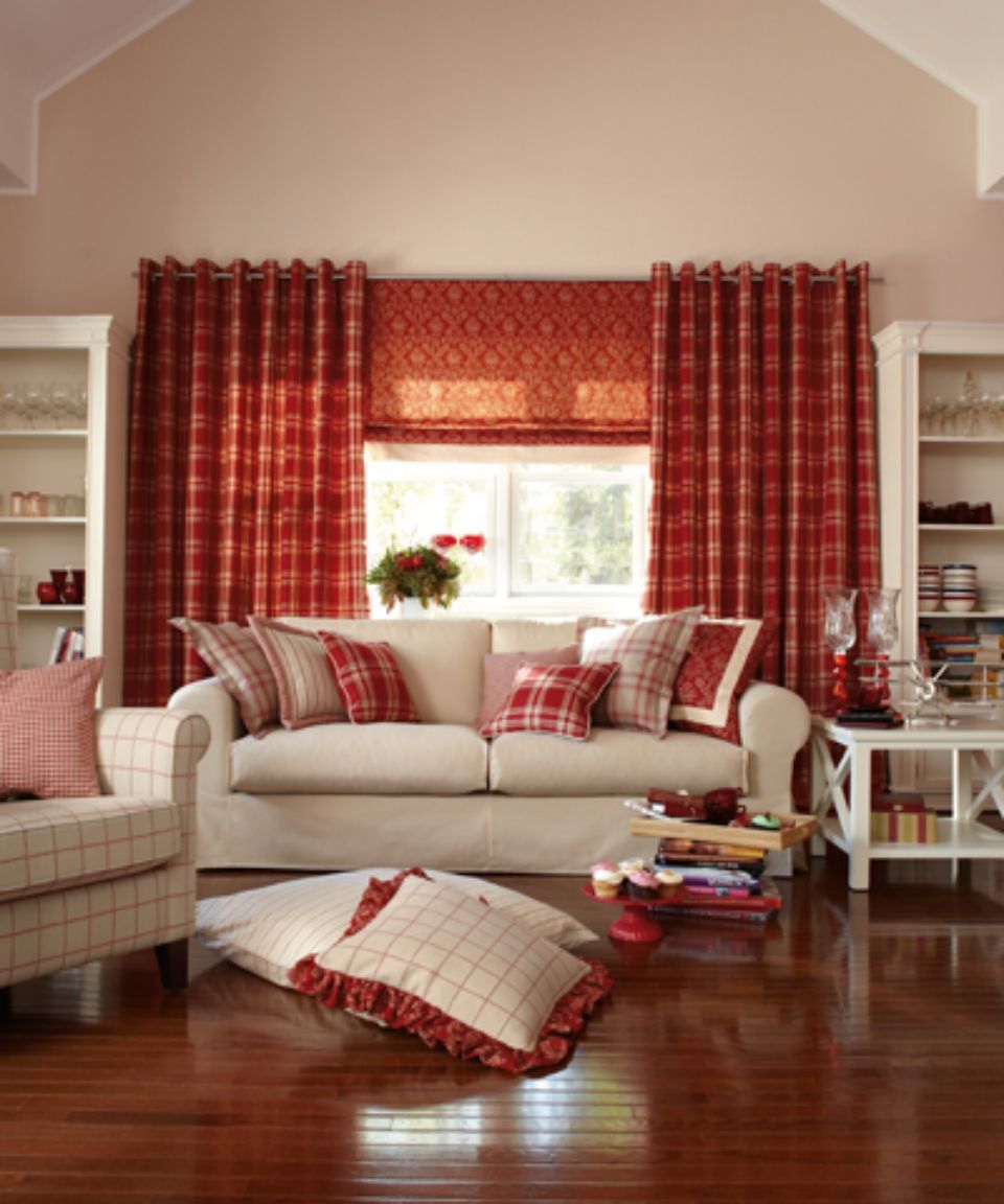 Accogliente soggiorno con divano bianco, cuscini a quadri, tende rosse e librerie integrate.