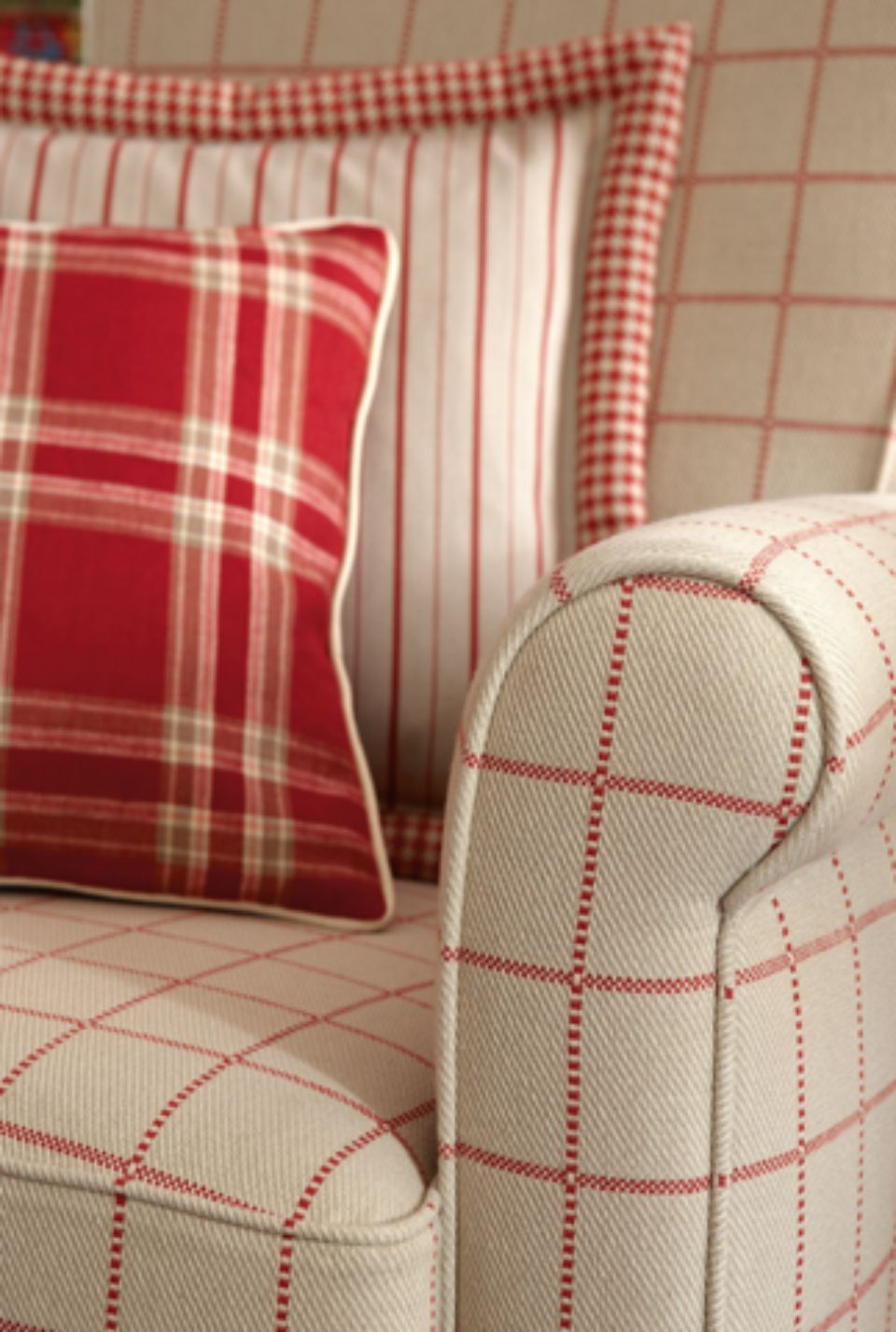 Primo piano di una poltrona color crema con tessuto a quadri rossi, due cuscini a quadri e un cuscino a righe.