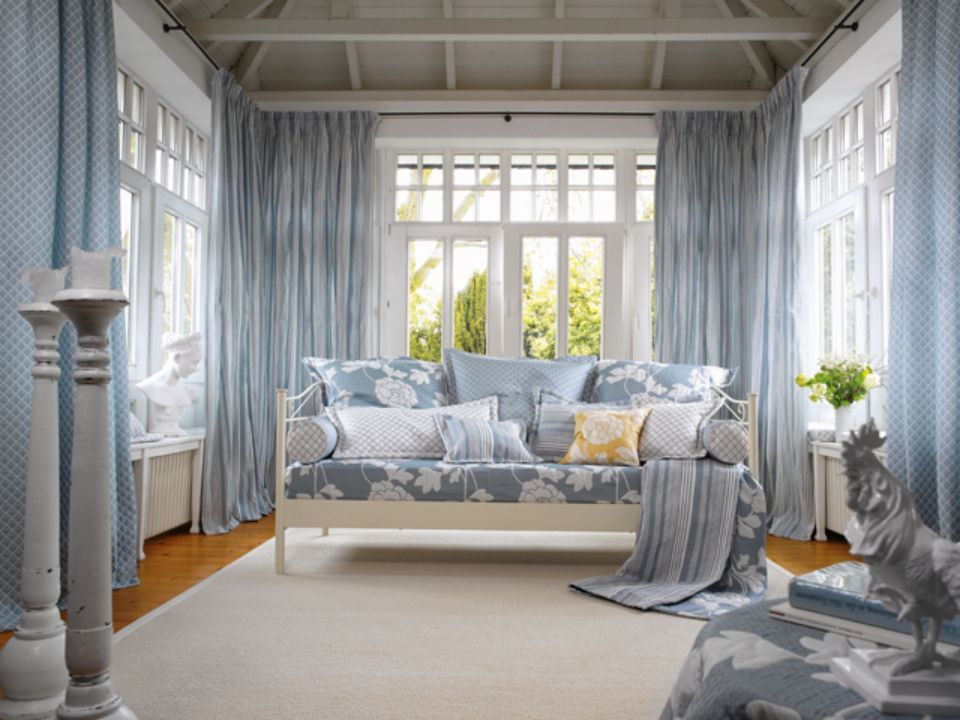 Veranda luminosa con decorazioni blu e bianche. Divano letto, tende e cuscini con motivi floreali.