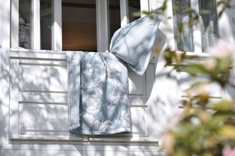 Coperta e cuscino drappeggiati su una finestra bianca con un disegno floreale, all'esterno.