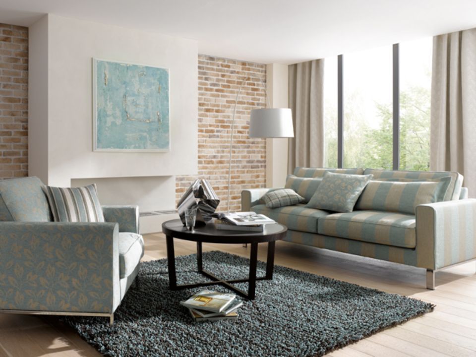 Soggiorno con divano a righe blu, poltrona, parete in mattoni e opere d'arte.