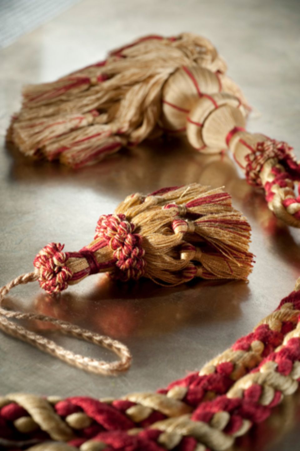 Primo piano di due nappe decorative in oro e rosso, adagiate su una superficie metallica.