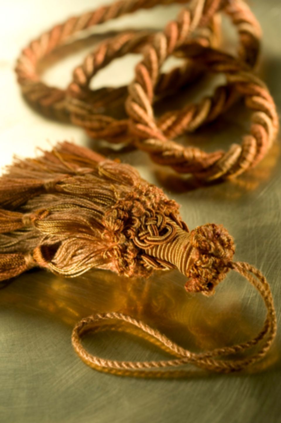 Corda con nappe nei toni dell'arancione e dell'oro su una superficie riflettente.