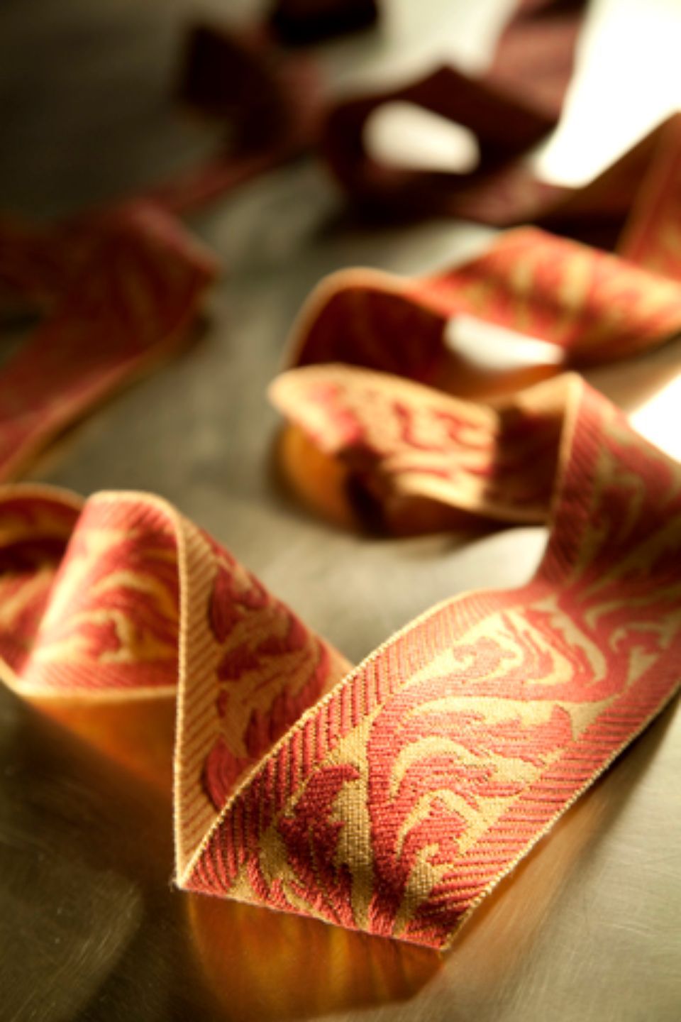 Nastro con motivi rossi e dorati adagiato su una superficie riflettente, illuminato da una luce soffusa.