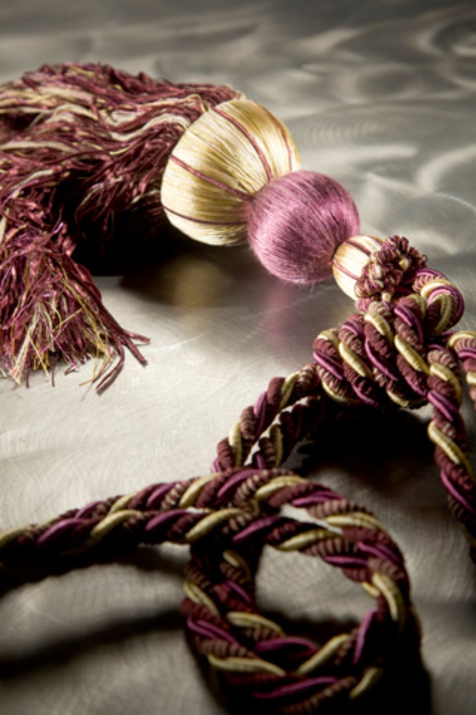 Nappa viola e oro con cordino spesso intrecciato, adagiata su una superficie argentata e testurizzata.