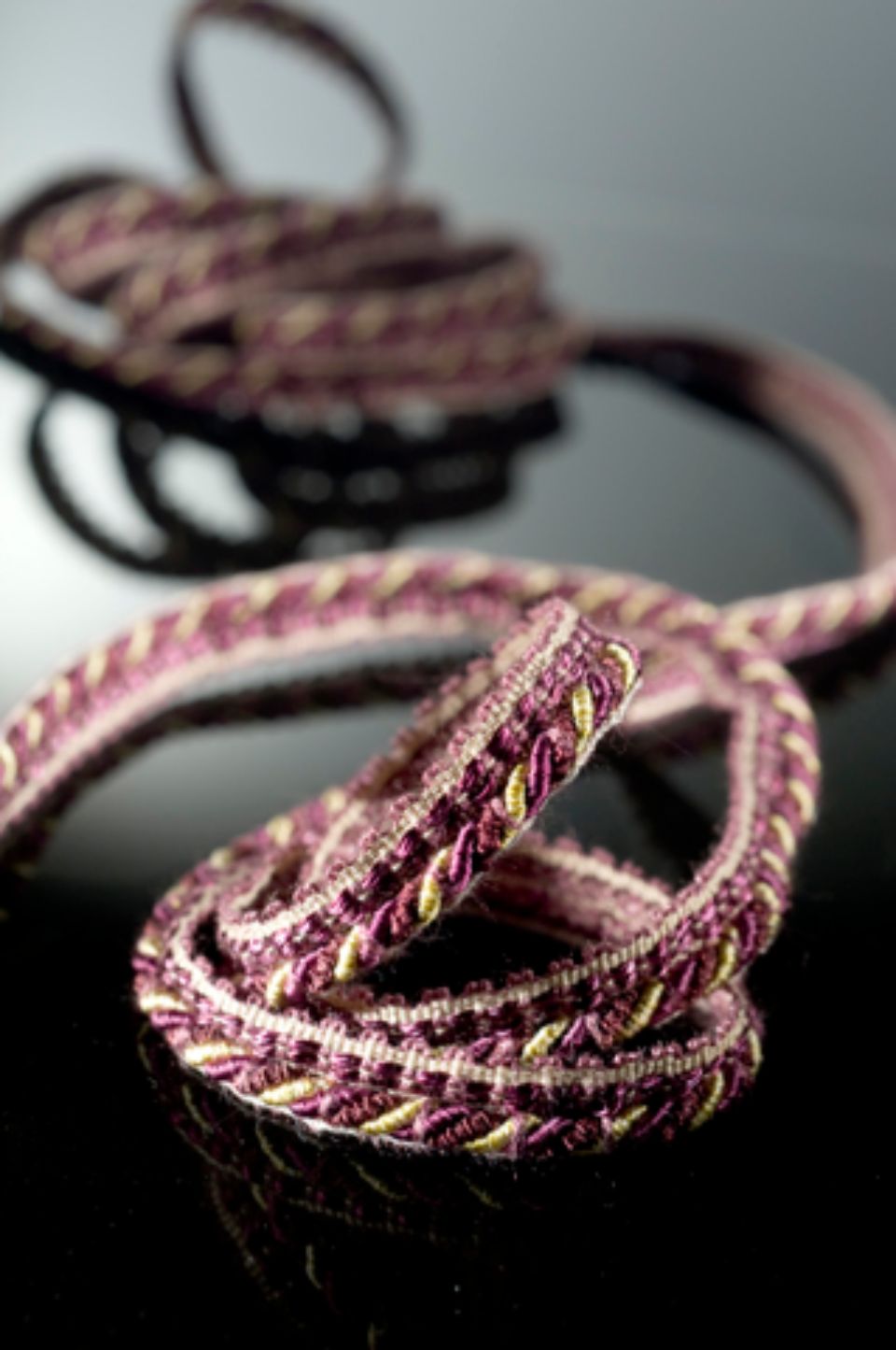 Passamaneria decorativa a spirale nelle tonalità del viola e dell'oro su una superficie nera riflettente.