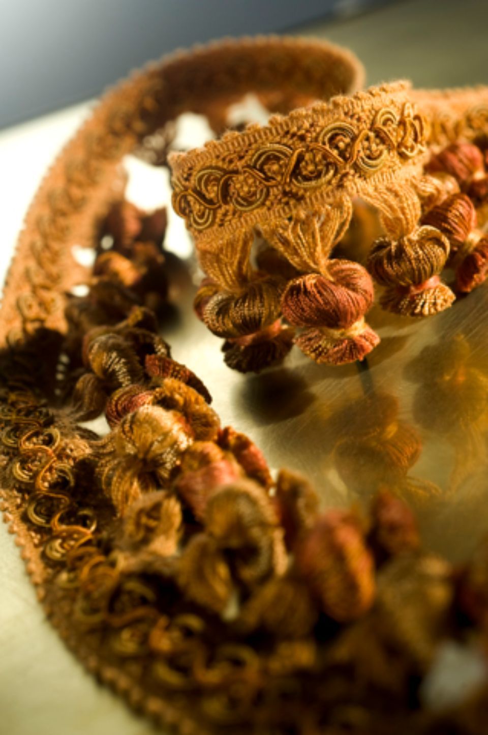 Primo piano di un elaborato bordo con nappe marroni e beige, probabilmente antico, su una superficie chiara.