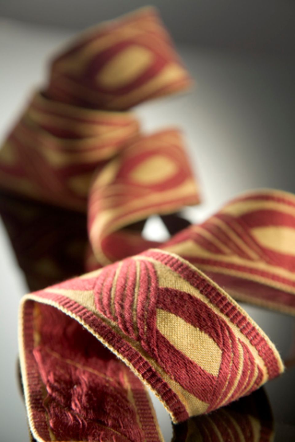 Nastro con motivo rosso e oro, arricciato su una superficie riflettente.