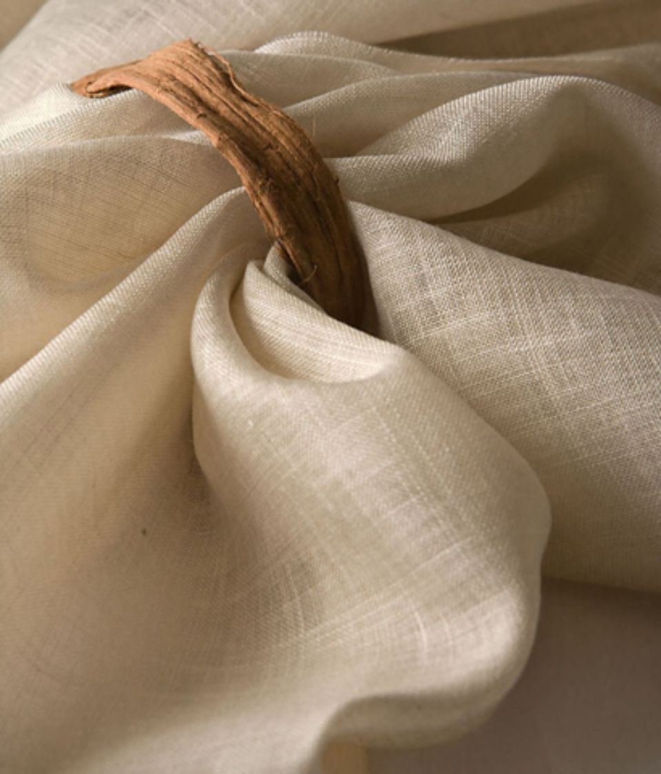 Tessuto di lino color crema drappeggiato attraverso un anello di legno, che mette in risalto morbide trame e pieghe.