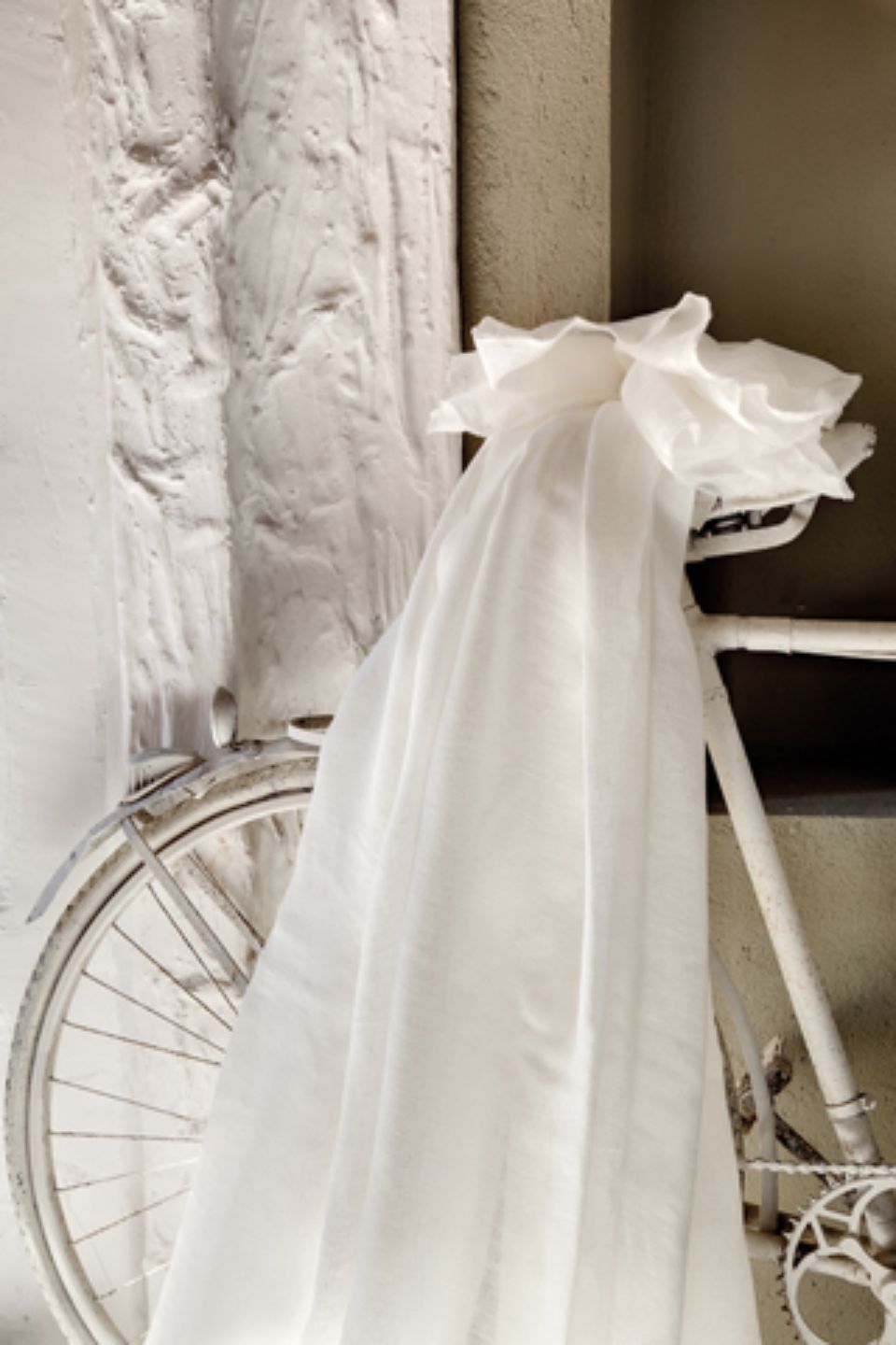 Bicicletta bianca ricoperta da un morbido tessuto bianco, appoggiata contro una parete bianca.