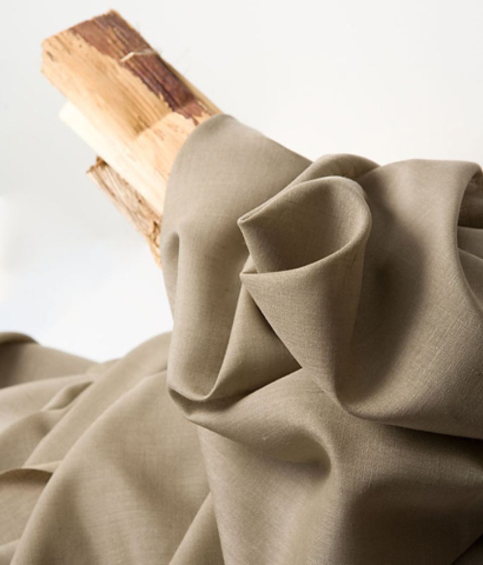 Tessuto color marrone chiaro drappeggiato su bastoncini di legno chiari, con il tessuto in morbide pieghe.