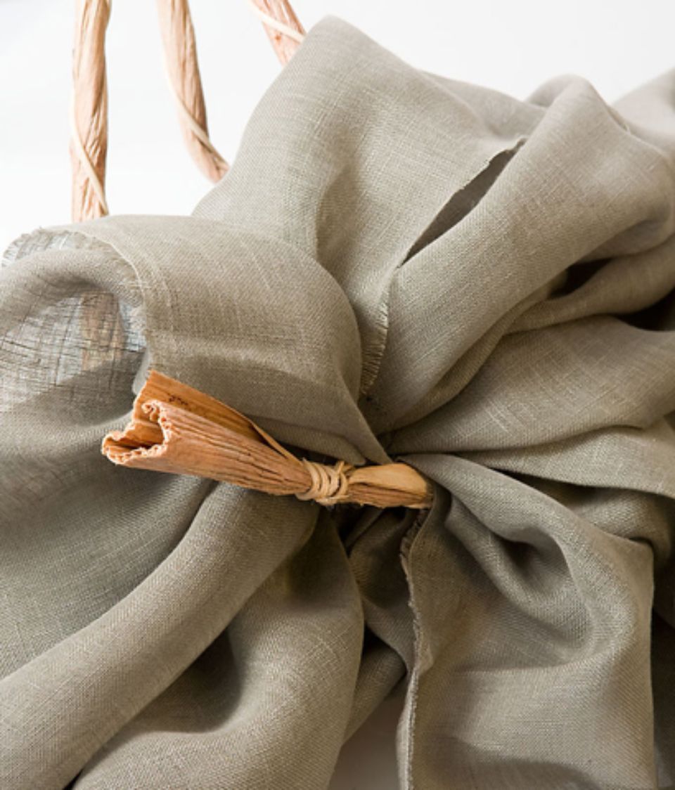 Sciarpa di lino beige chiusa con una fibbia di legno e appoggiata su un manico intrecciato.