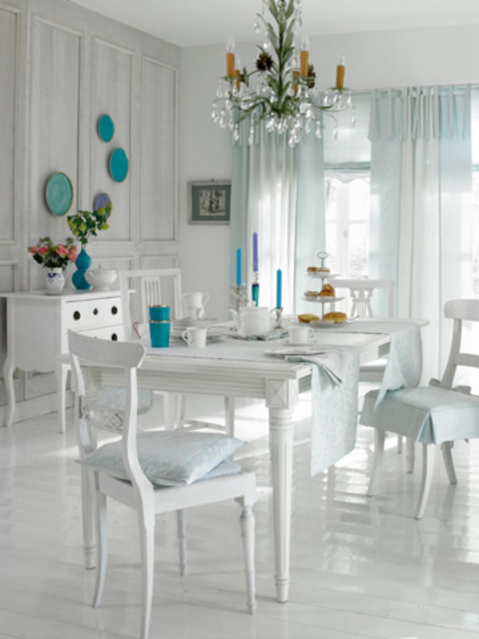 Sala da pranzo bianca con tavolo, sedie, lampadario e dettagli azzurri.