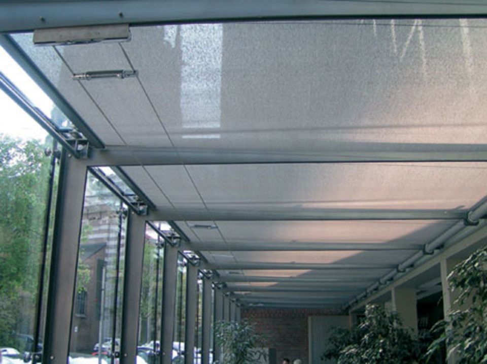 Passaggio coperto con pareti in vetro, struttura in metallo e soffitto in tessuto. Piante che rivestono l'interno.