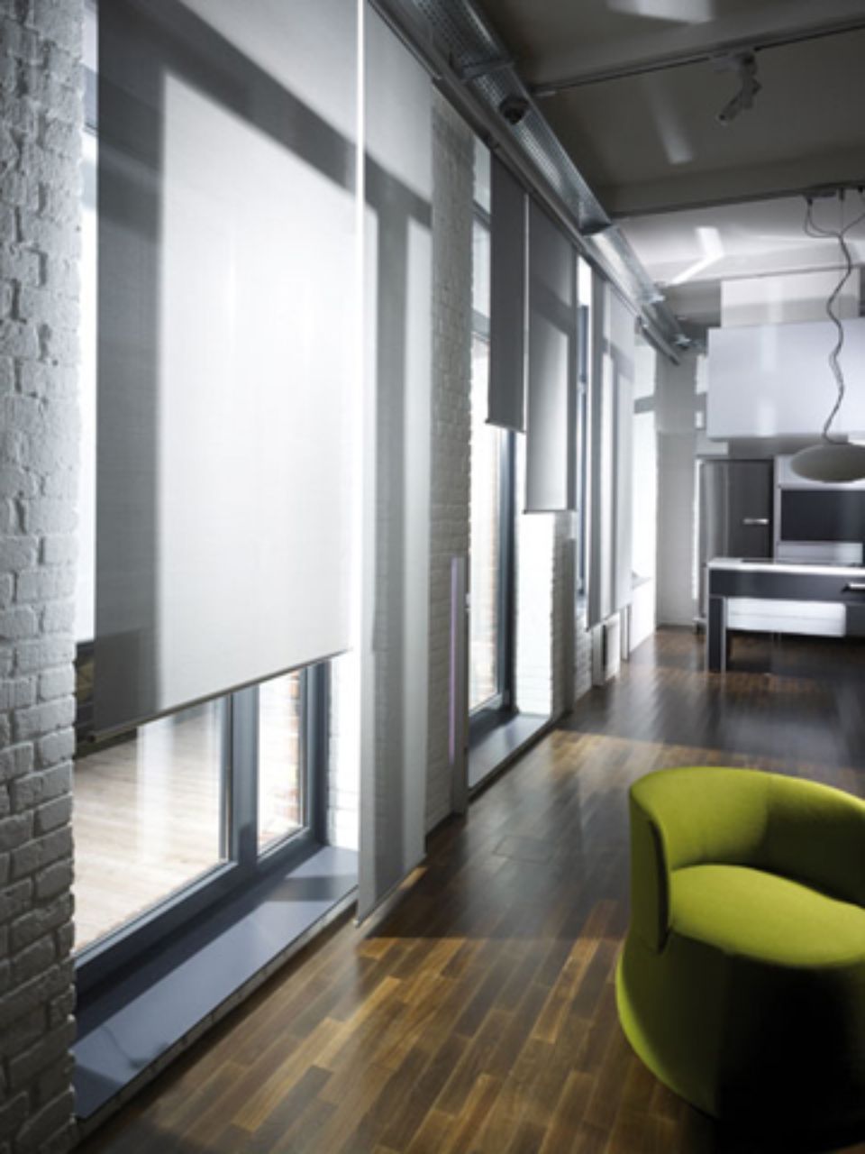 Interni moderni con lunghe finestre, tende bianche, mattoni a vista e una poltrona verde.