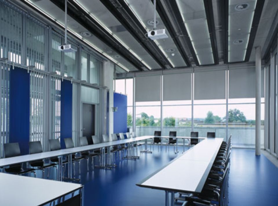 Moderna sala conferenze con pavimento blu, lungo tavolo, sedie e ampie finestre.