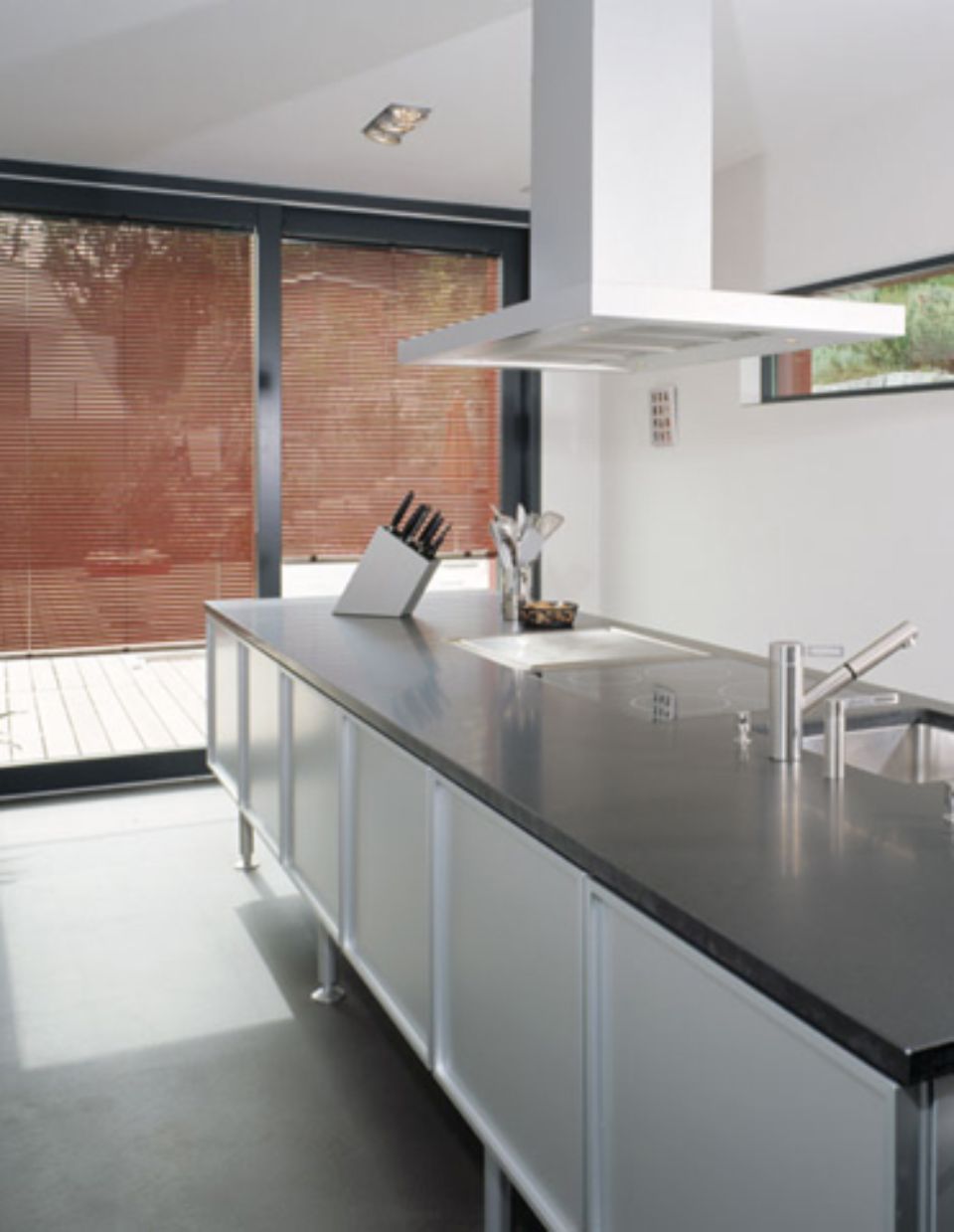 Cucina moderna con isola, elettrodomestici in acciaio inossidabile, ripiani neri e finestra con persiane.