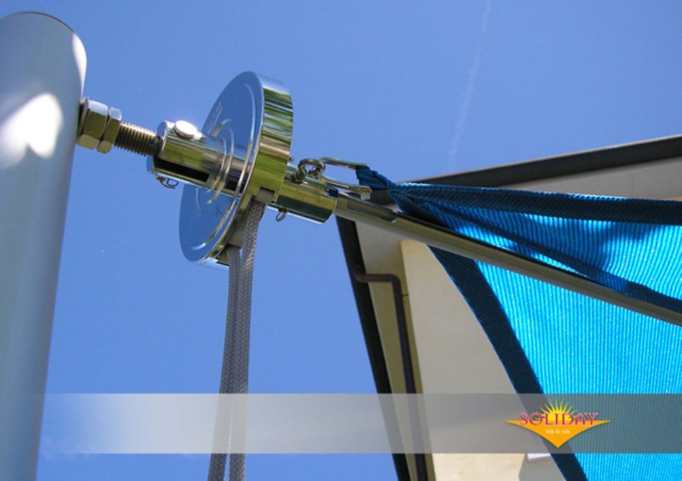 Elementi metallici che fissano una vela parasole blu a un palo bianco sotto un cielo azzurro.