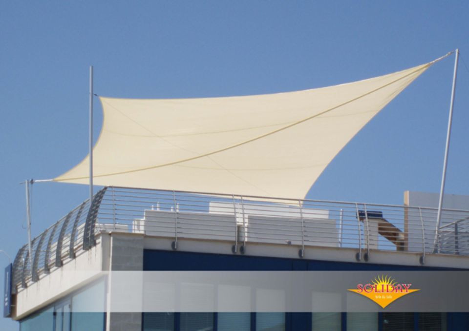 Una vela ombreggiante rettangolare color crema, fissata al tetto di un edificio, che fornisce protezione dal sole.